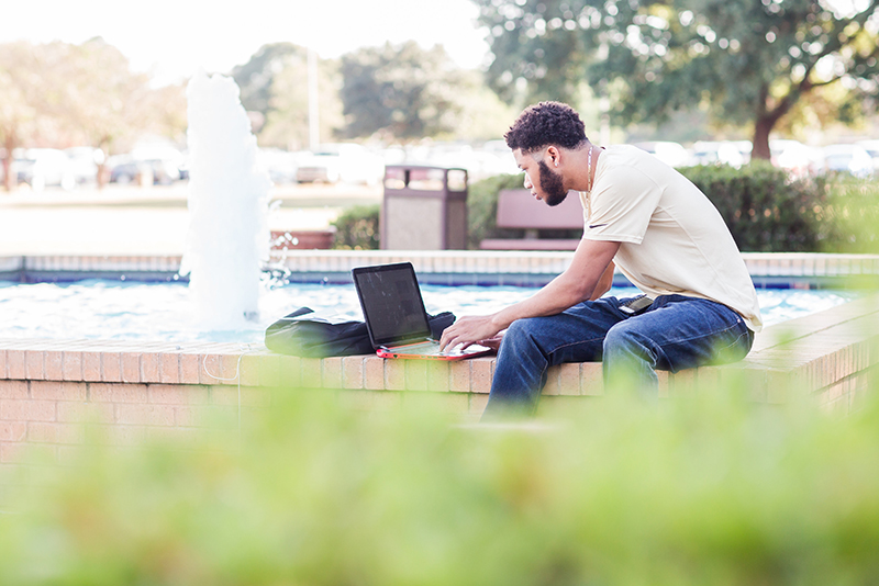 Photo of student using laptop computer by fountain